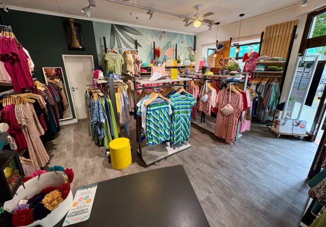 Buntes Modegeschäft mit Kleidung auf Kleiderständern und einem gelben Hocker.